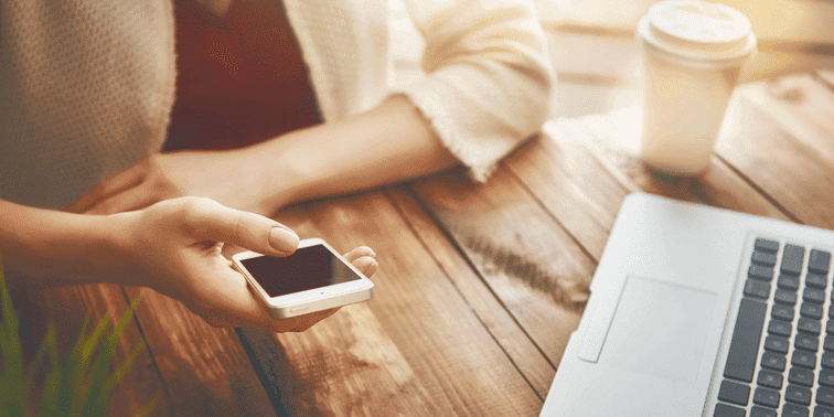 Person holding smartphone beside laptop on wooden table, symbolising digital marketing and online presence.