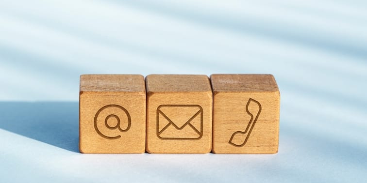 Wooden blocks displaying contact symbols: @ symbol, email envelope, and telephone receiver, representing communication methods for effective email marketing strategies.