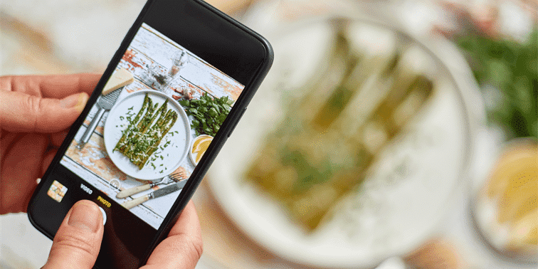 Person photographing a plate of grilled asparagus with herbs and lemon, showcasing food photography for digital marketing.