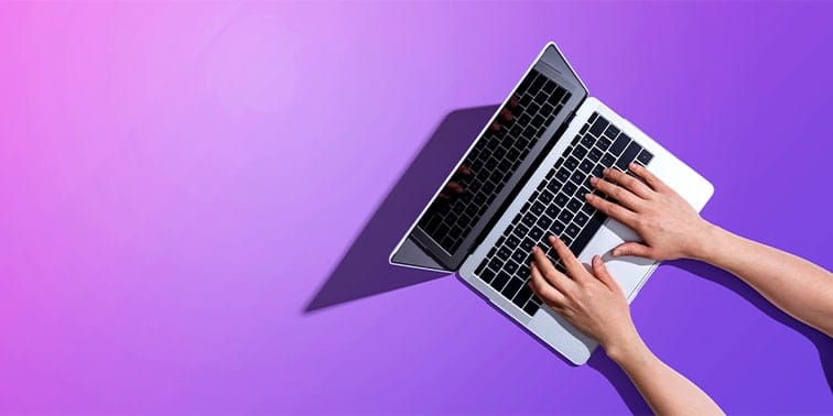 Hands typing on a laptop against a vibrant purple background, symbolising digital marketing and online presence enhancement.