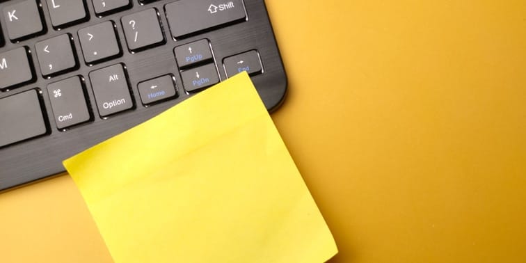 Wireless keyboard with a yellow sticky note on a vibrant orange background, symbolising digital marketing and productivity.