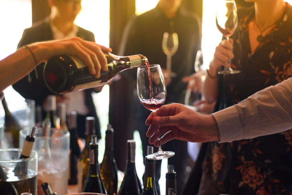 Wine being poured into a glass at a networking event, surrounded by attendees enjoying wine tasting at The Jolly Farmers pub.