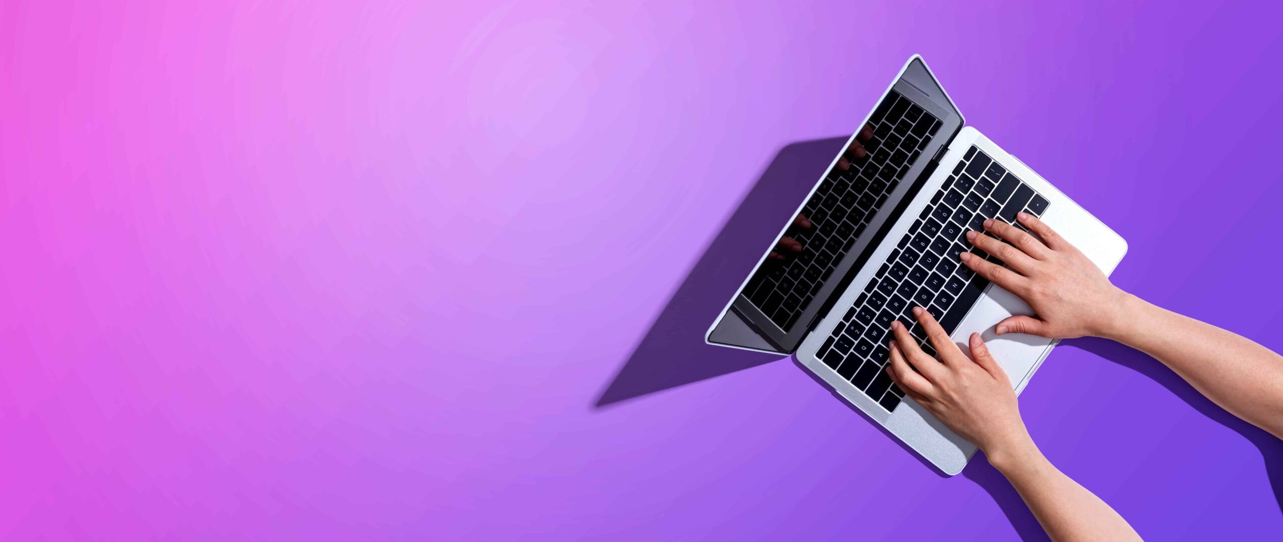 Hands typing on a laptop against a vibrant purple background, representing digital marketing and online business strategies.