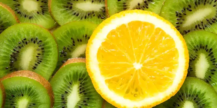 Sliced kiwi fruit arranged around a halved orange, showcasing vibrant colours and textures, representing fresh produce and healthy eating.