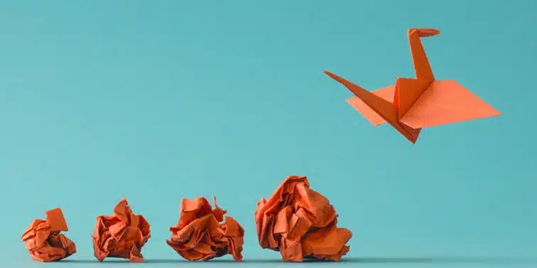 Orange origami crane flying above crumpled orange paper, symbolising creativity and transformation in digital marketing for small businesses.