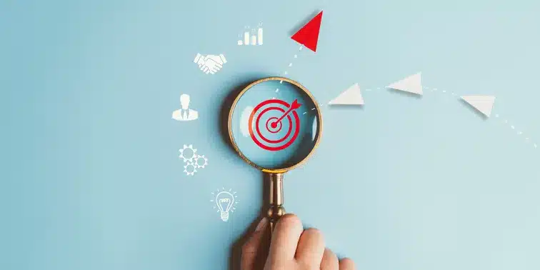 Hand holding magnifying glass focusing on a target symbol, with icons representing business growth, strategy, and digital marketing elements.