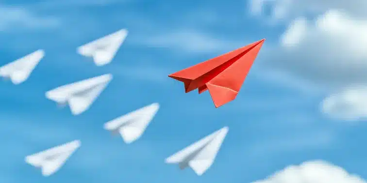 Red paper plane leading a group of white paper planes against a blue sky, symbolising innovative digital marketing trends for small businesses.