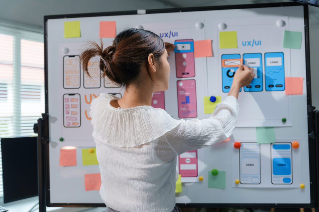 Website designer improving user experience on mobile app wireframe using whiteboard and colorful sticky notes in office